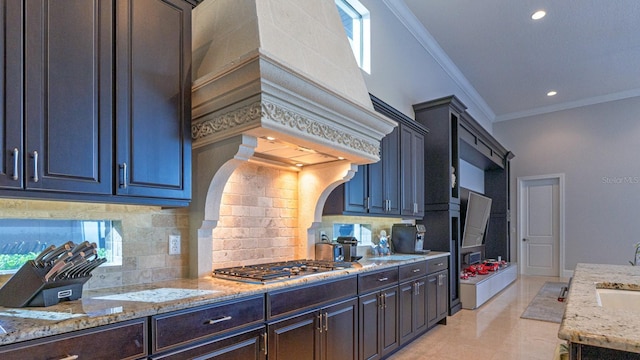 kitchen with light stone counters, ornamental molding, custom exhaust hood, decorative backsplash, and stainless steel gas stovetop