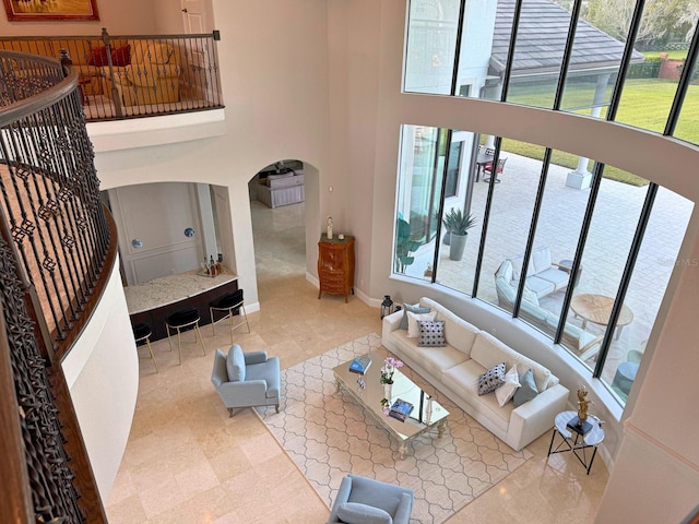 living area with arched walkways, a towering ceiling, baseboards, and stairs