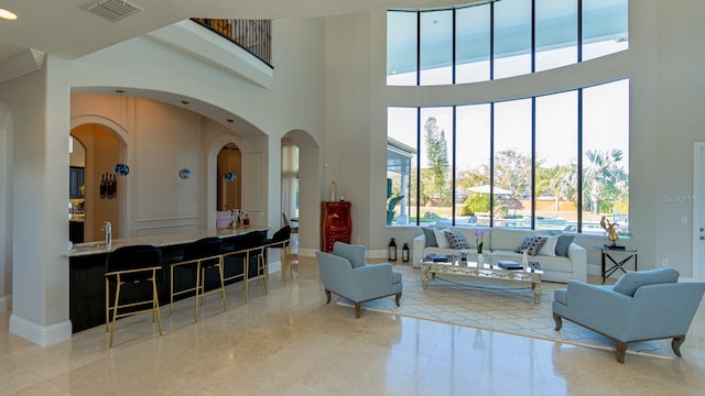 living room featuring arched walkways, visible vents, a towering ceiling, and baseboards