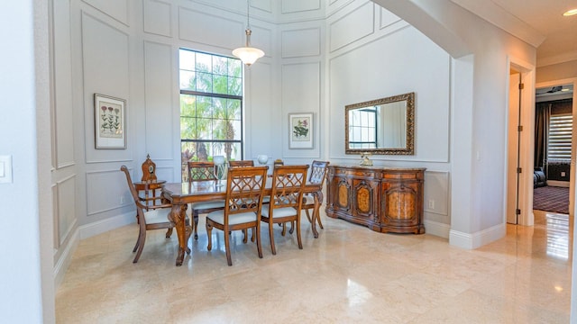 dining room featuring arched walkways, a decorative wall, and ornamental molding