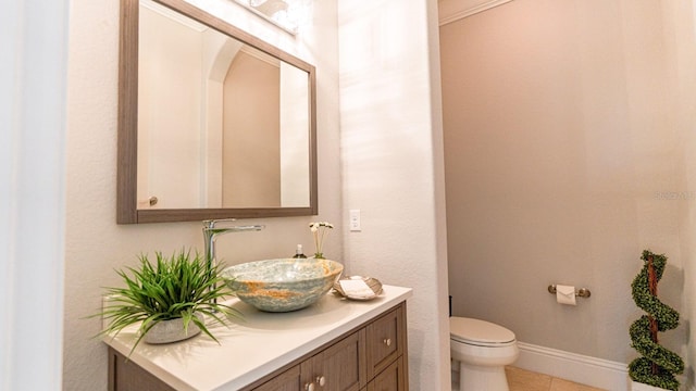 half bath with toilet, tile patterned flooring, baseboards, and vanity