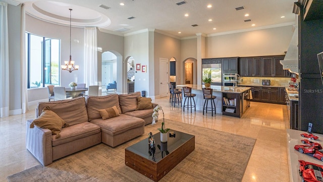 living area with arched walkways, crown molding, visible vents, a towering ceiling, and a chandelier