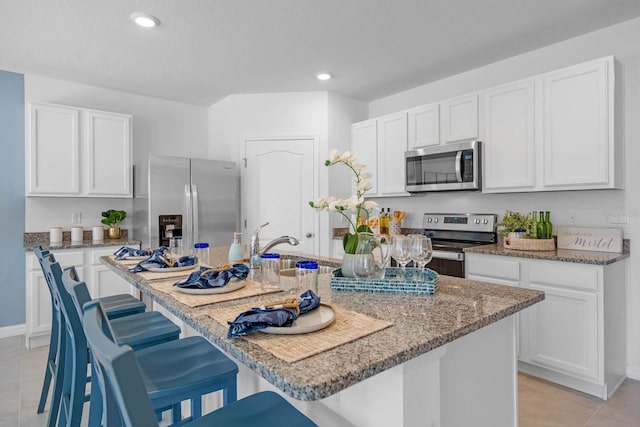 kitchen featuring a breakfast bar area, appliances with stainless steel finishes, stone countertops, white cabinets, and a kitchen island with sink