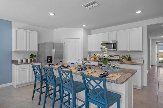 kitchen with a center island with sink, visible vents, white cabinets, a breakfast bar area, and stainless steel appliances