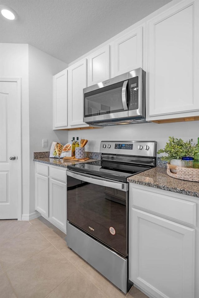 kitchen with white cabinets, appliances with stainless steel finishes, dark stone countertops, a textured ceiling, and light tile patterned flooring