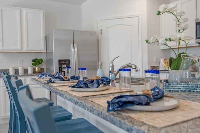 kitchen with a breakfast bar, stainless steel refrigerator with ice dispenser, white cabinets, a sink, and light stone countertops