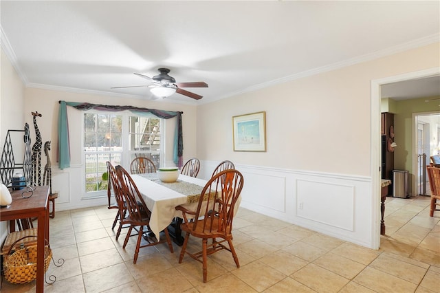 dining room featuring light tile patterned floors, a wainscoted wall, ceiling fan, crown molding, and a decorative wall