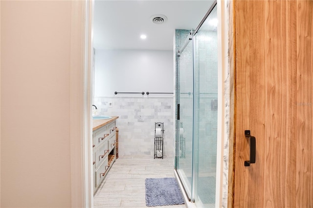 bathroom with visible vents, a shower stall, tile walls, and vanity