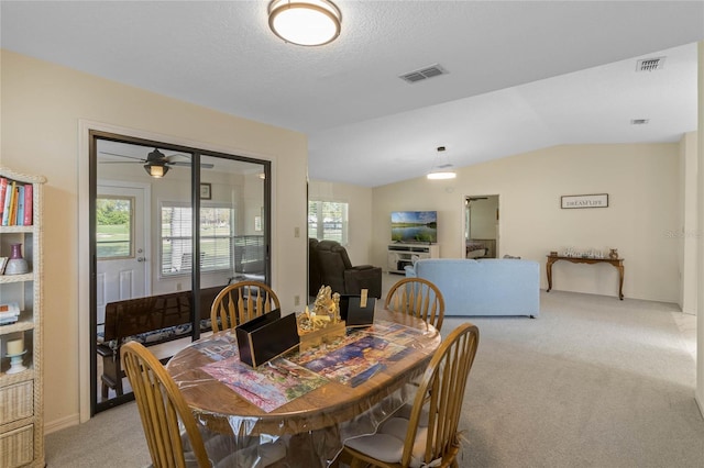 dining space with a textured ceiling, visible vents, light colored carpet, and vaulted ceiling