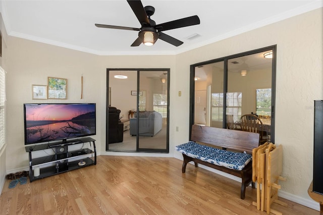 living area with visible vents, ornamental molding, light wood finished floors, baseboards, and ceiling fan