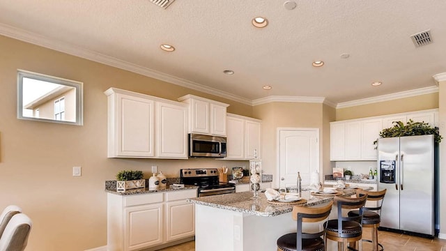 kitchen with stainless steel appliances, a kitchen bar, a center island with sink, and white cabinets