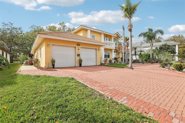 mediterranean / spanish home featuring stucco siding, decorative driveway, a front yard, an attached garage, and a balcony