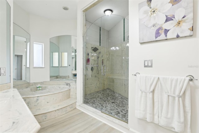 full bath featuring vanity, a bath, wood finished floors, and a marble finish shower