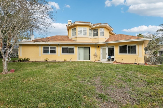 view of front of property with stucco siding, a tiled roof, a front lawn, and a chimney