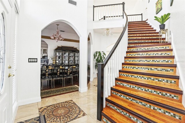 tiled foyer entrance with visible vents, a notable chandelier, arched walkways, baseboards, and stairs