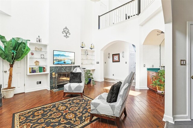 living room featuring baseboards, arched walkways, wood finished floors, and a fireplace