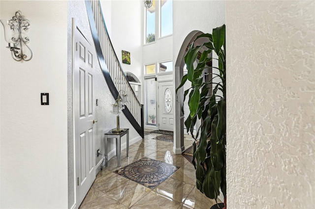 entrance foyer featuring stairway, baseboards, a high ceiling, a textured wall, and marble finish floor