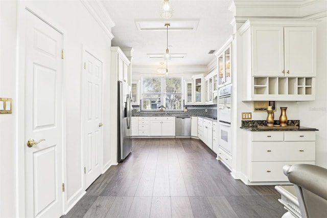 kitchen with a sink, dark countertops, dark wood-style floors, stainless steel appliances, and glass insert cabinets