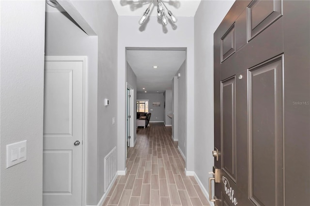 corridor featuring visible vents, baseboards, light wood-style floors, and an inviting chandelier