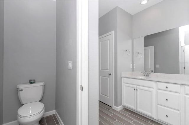 bathroom with wood finish floors, baseboards, toilet, and vanity