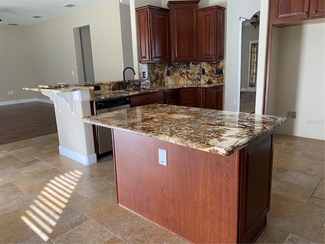 kitchen featuring stone tile flooring, backsplash, stainless steel dishwasher, a sink, and a peninsula