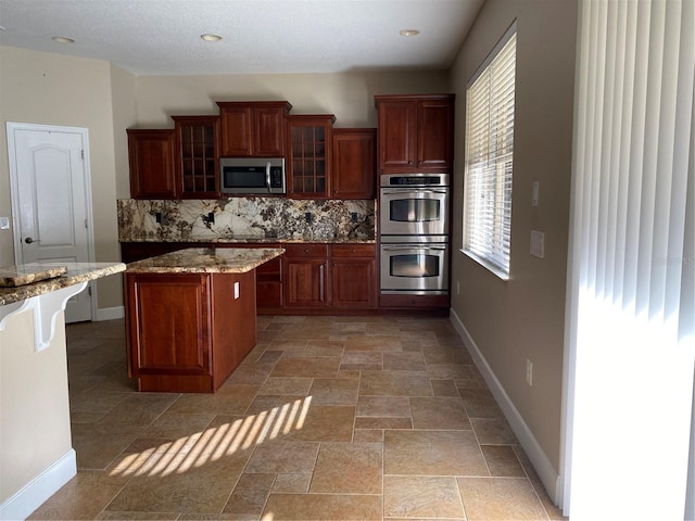 kitchen featuring a kitchen island, baseboards, stainless steel appliances, and decorative backsplash