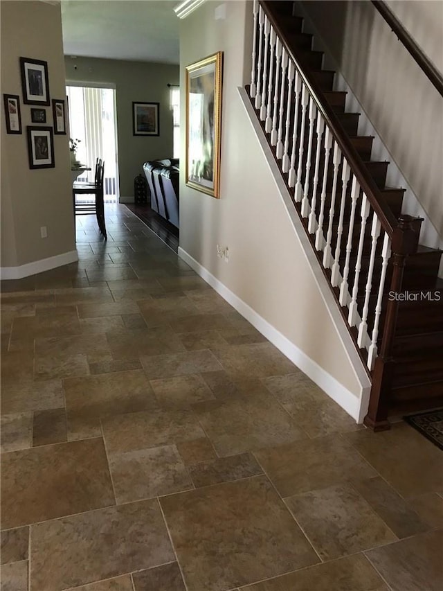 corridor with stairs, stone finish flooring, and baseboards