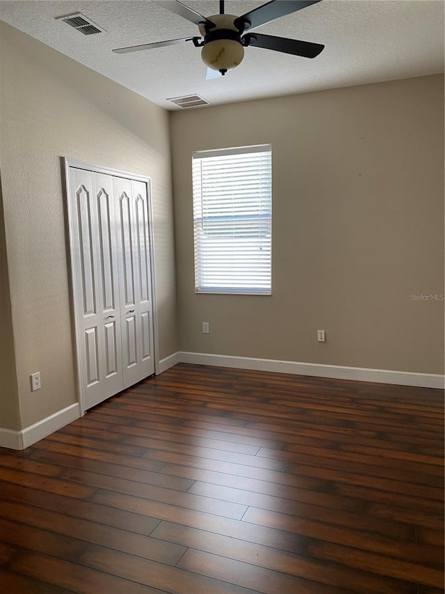 unfurnished bedroom featuring dark wood-style floors, baseboards, visible vents, and a closet