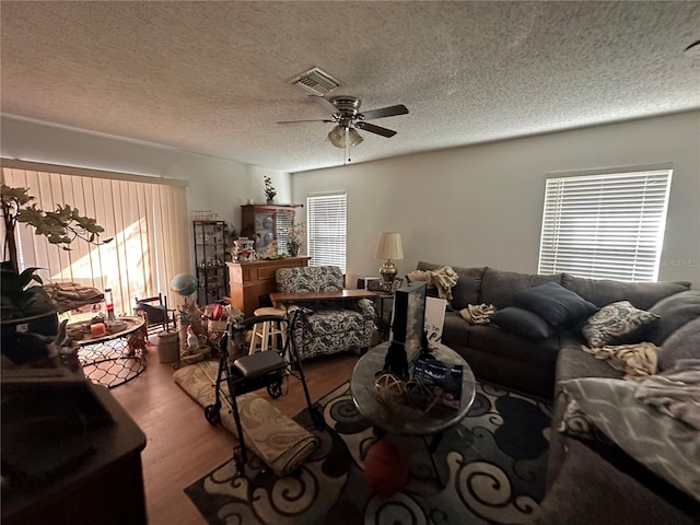 living area featuring a ceiling fan, visible vents, a textured ceiling, and wood finished floors