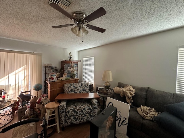 living area with a ceiling fan, visible vents, a textured ceiling, and wood finished floors