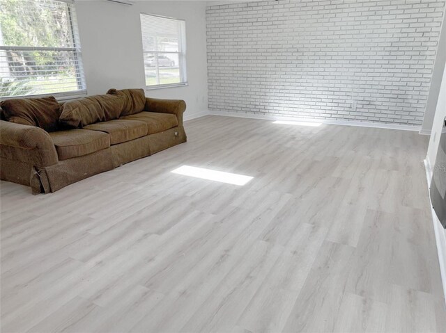 living area with light wood finished floors, brick wall, baseboards, and a wealth of natural light