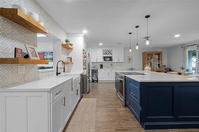 kitchen with open shelves, blue cabinetry, a sink, and stainless steel appliances