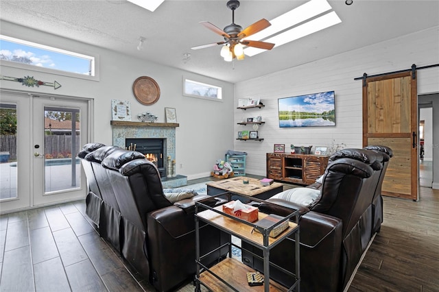 living room featuring a tile fireplace, wood finished floors, ceiling fan, and a barn door