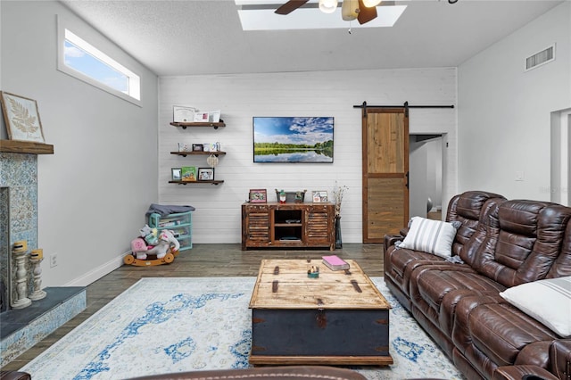 living room with a barn door, visible vents, a tile fireplace, ceiling fan, and wood finished floors