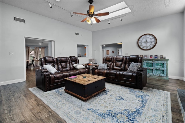 living room with a skylight, a ceiling fan, wood finished floors, rail lighting, and a textured ceiling