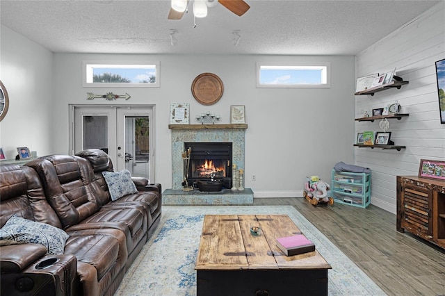 living area featuring a tiled fireplace, a ceiling fan, wood finished floors, a textured ceiling, and french doors