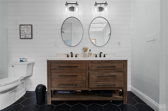 bathroom featuring toilet, double vanity, a sink, and tile patterned floors