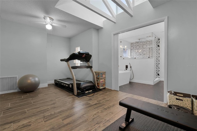 exercise area featuring ceiling fan, a skylight, wood finished floors, visible vents, and baseboards