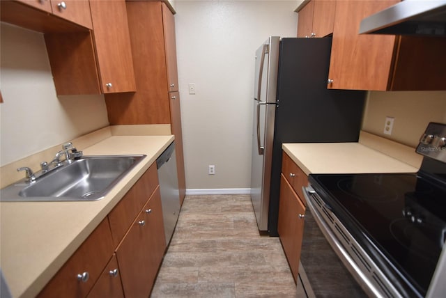 kitchen featuring under cabinet range hood, a sink, light countertops, appliances with stainless steel finishes, and brown cabinetry