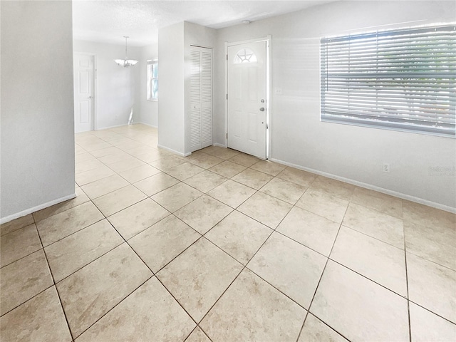 tiled entrance foyer with an inviting chandelier and baseboards