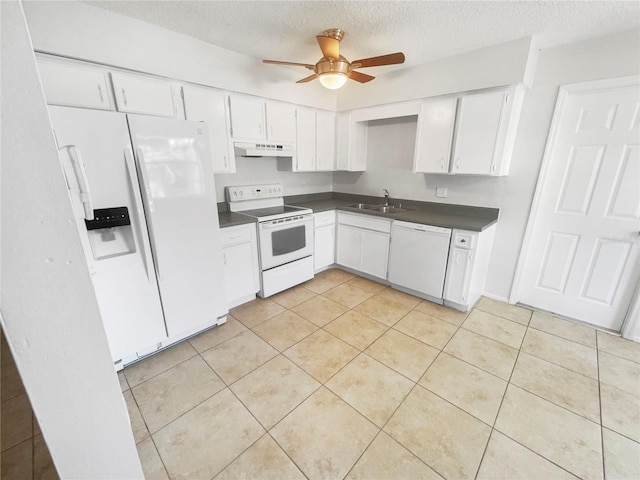 kitchen featuring white appliances, white cabinets, dark countertops, under cabinet range hood, and a sink