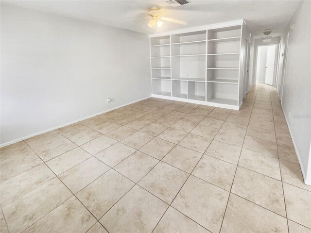 empty room featuring light tile patterned flooring, a ceiling fan, baseboards, visible vents, and built in features