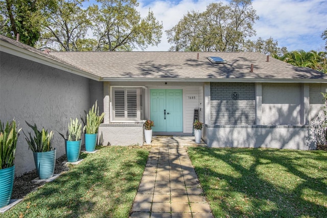 view of exterior entry with roof with shingles, brick siding, a lawn, and stucco siding