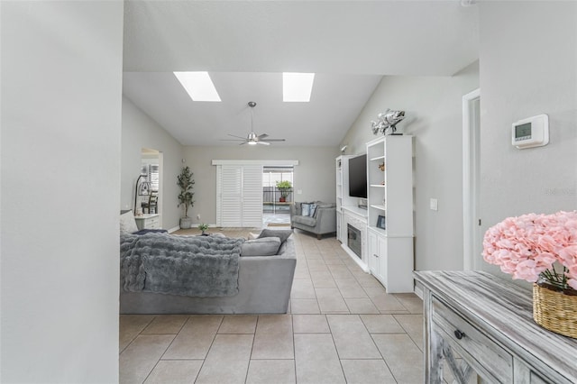 living area with a ceiling fan, vaulted ceiling with skylight, a glass covered fireplace, and light tile patterned floors