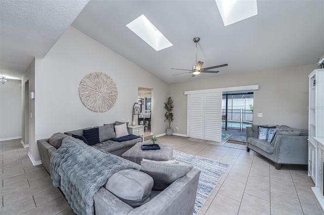 living room featuring vaulted ceiling with skylight, baseboards, a ceiling fan, and light tile patterned flooring