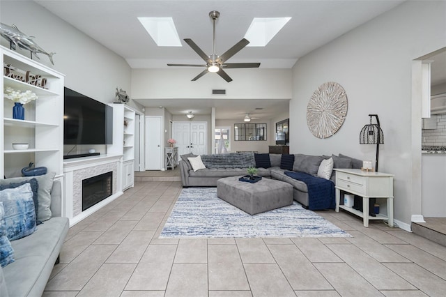 living room with vaulted ceiling with skylight, light tile patterned flooring, visible vents, and a ceiling fan