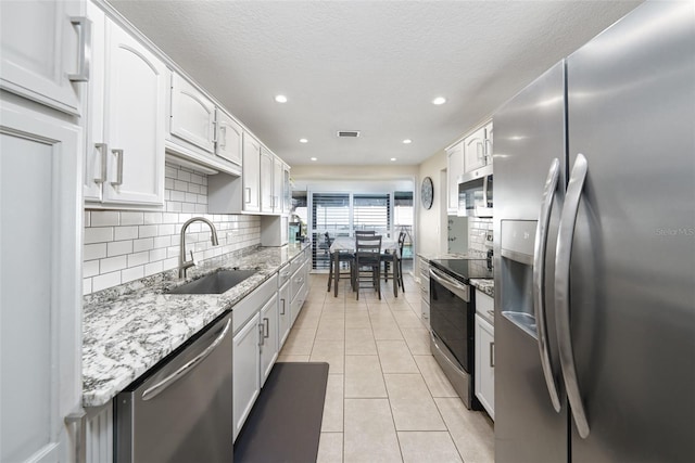 kitchen with light tile patterned floors, stainless steel appliances, a sink, and light stone countertops