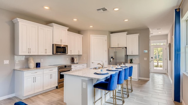 kitchen with visible vents, appliances with stainless steel finishes, a kitchen bar, white cabinetry, and a sink