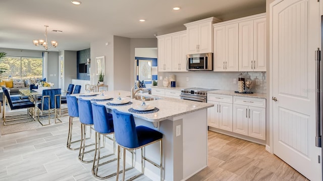 kitchen with an island with sink, a sink, light stone countertops, stainless steel appliances, and backsplash