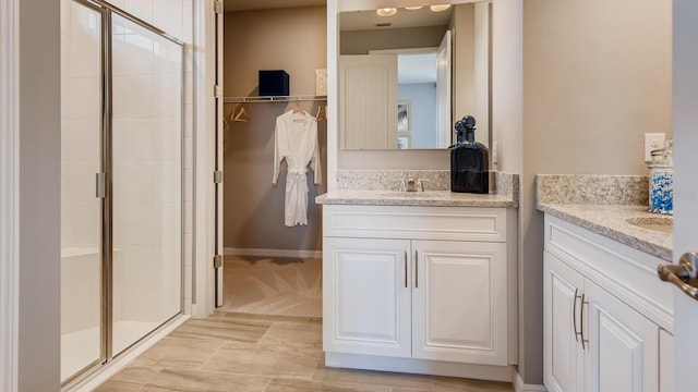 bathroom featuring a sink, a shower stall, baseboards, and two vanities